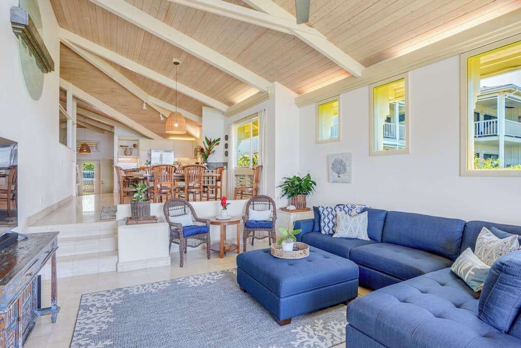 A spacious living room with a blue sofa, wooden ceiling beams, and a view of the outside balcony.
