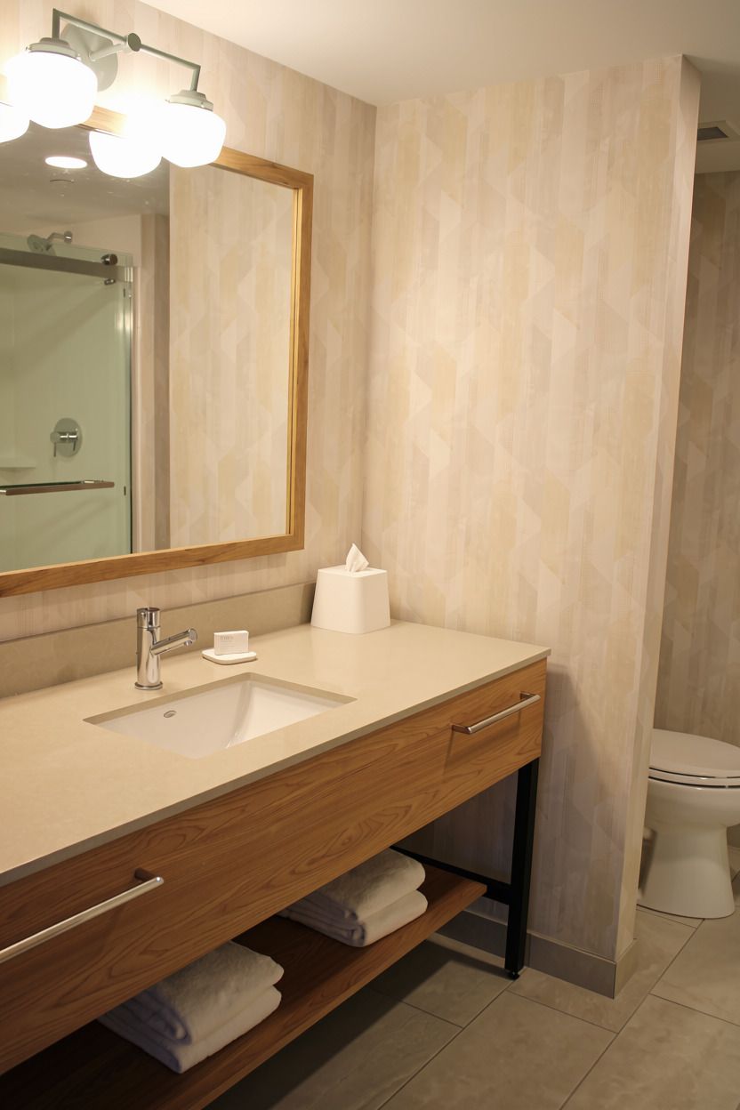 Un baño moderno con un espejo grande, un lavabo, un inodoro y un estante para toallas.