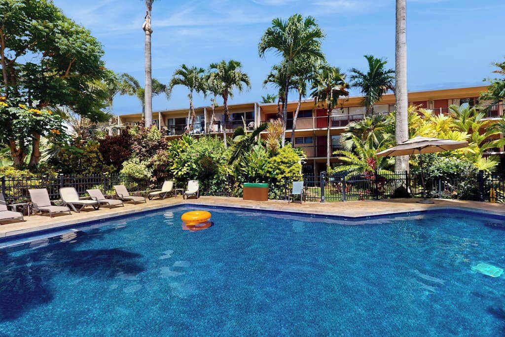 A swimming pool with lounge chairs, palm trees, and a building with balconies in the background.