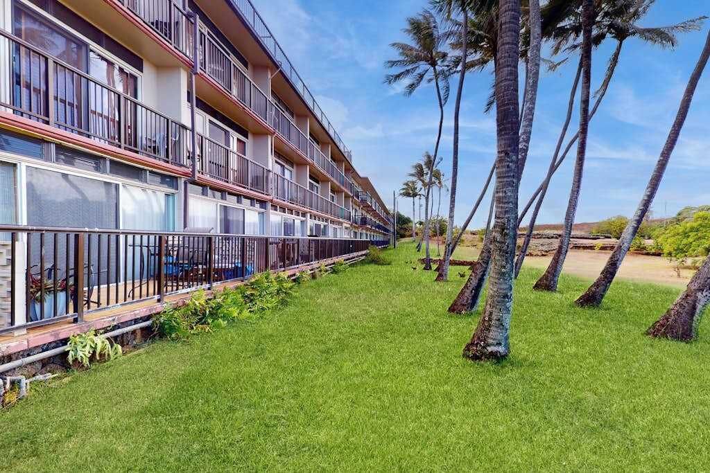 Un hotel de diverses plantes amb balcons, un jardí amb gespa i palmeres.