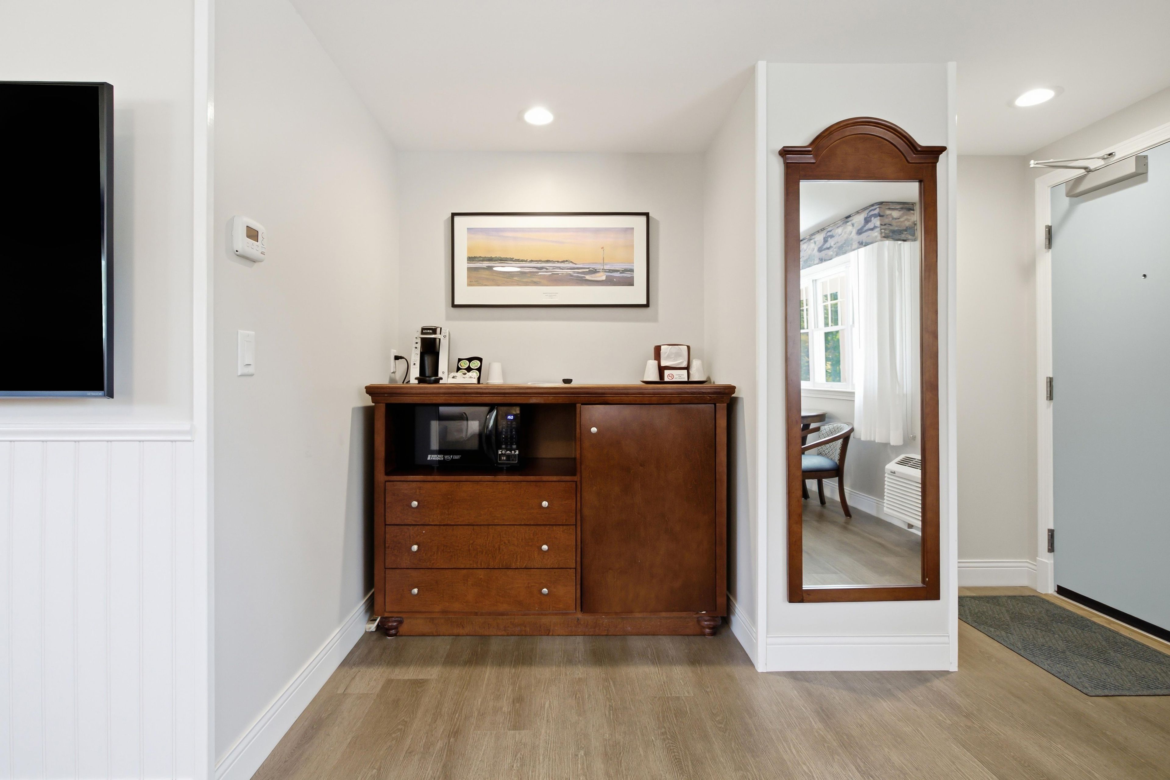 Une chambre d’hôtel avec une commode en bois, un tableau encadré au mur et un miroir avec un cadre en bois.