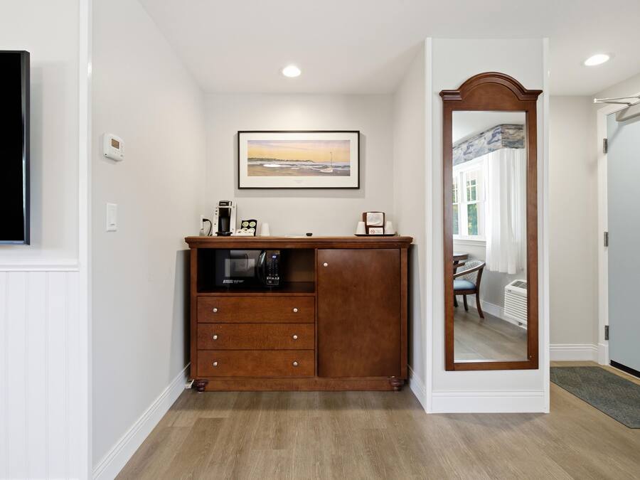 A hotel room with a wooden dresser, a framed picture on the wall, and a mirror with a wooden frame.