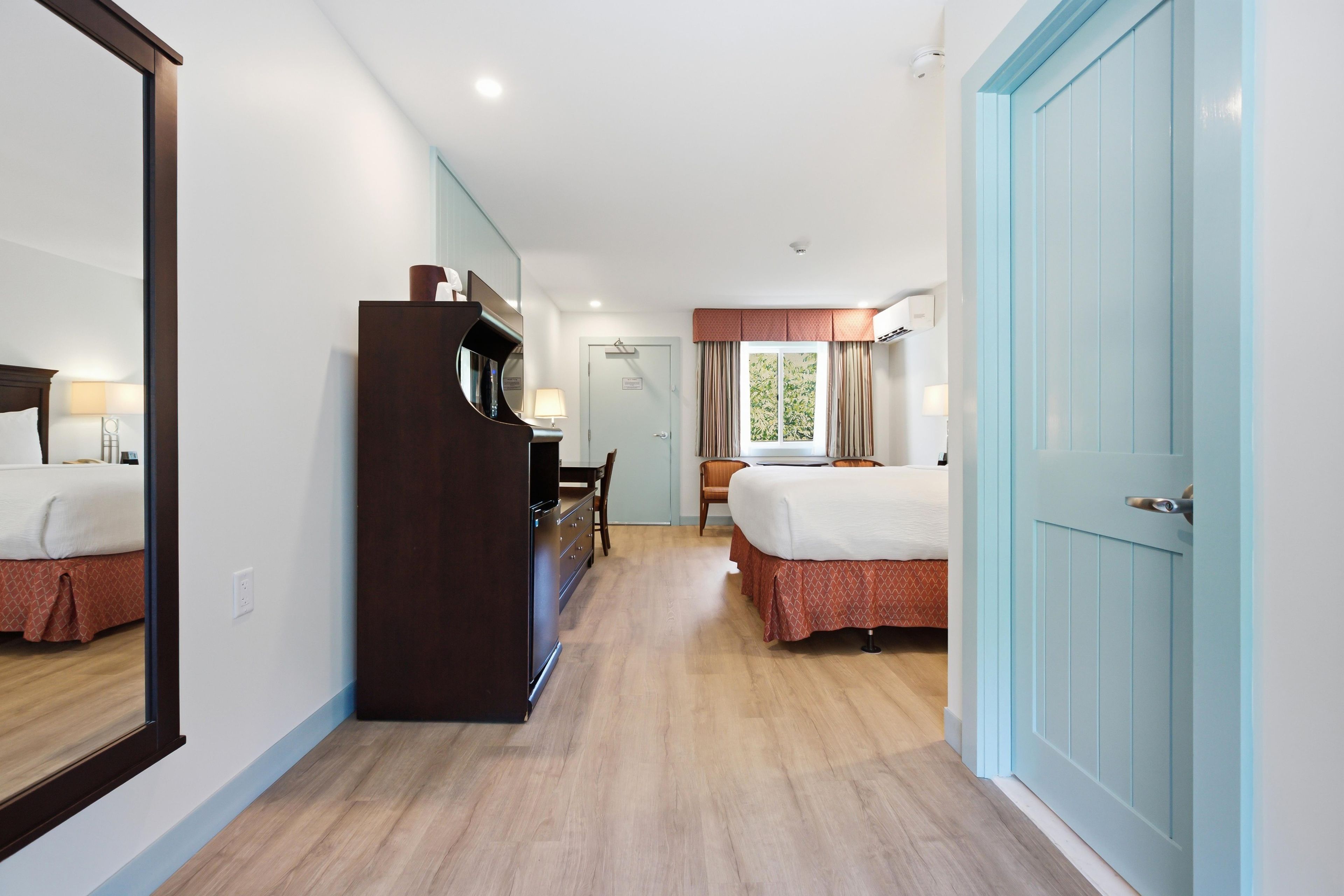 Una habitación de hotel con un espejo grande, un armario, un escritorio con silla y dos camas.