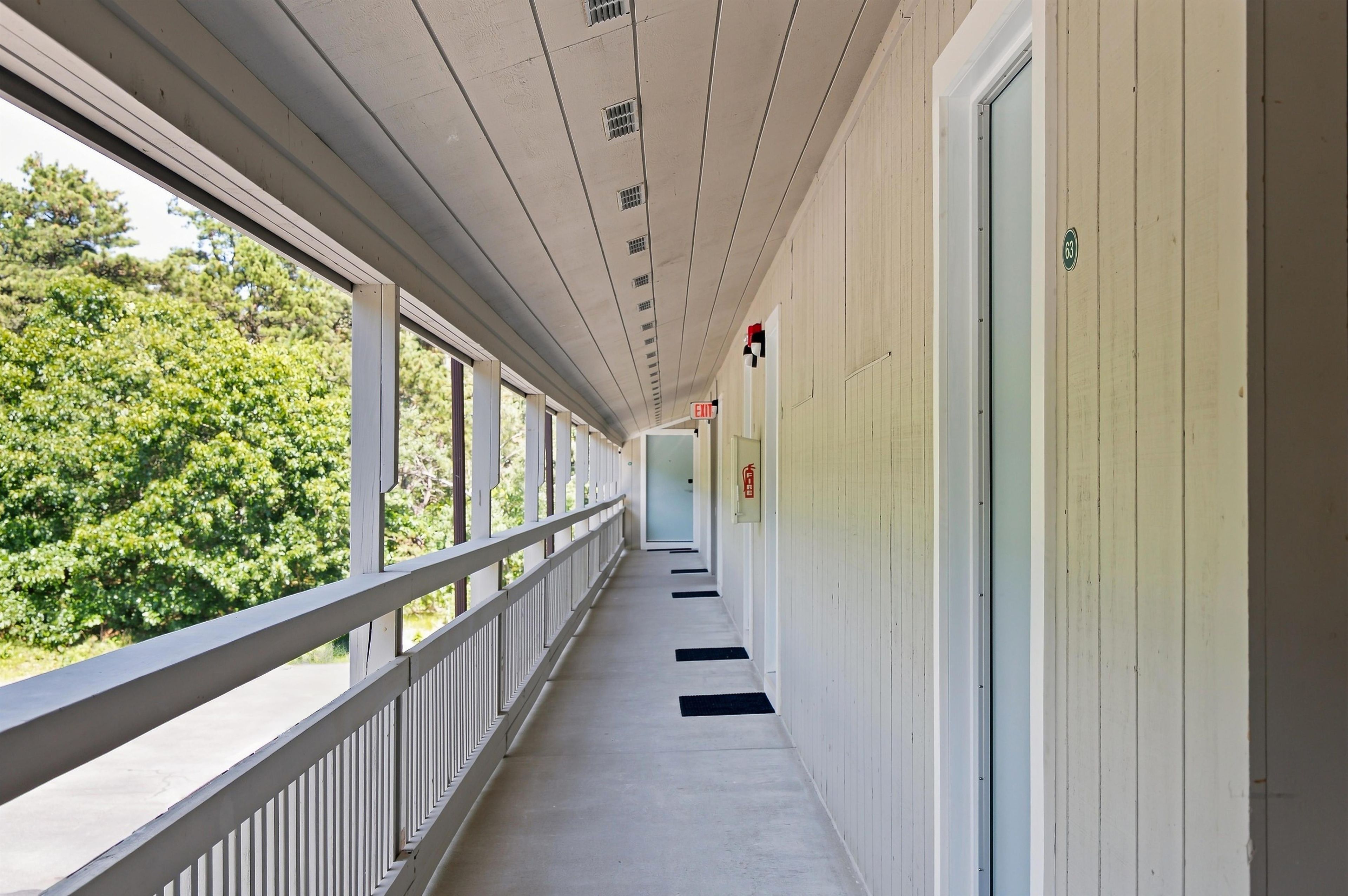 A corridor with a railing, a fire exit sign, and a door with a number.