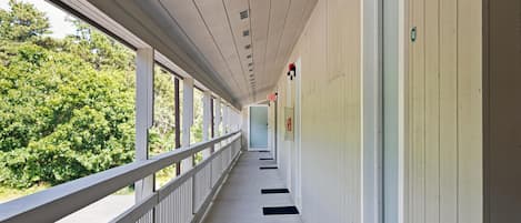 Un couloir avec une rambarde, un panneau indiquant la sortie de secours et une porte portant un numéro.