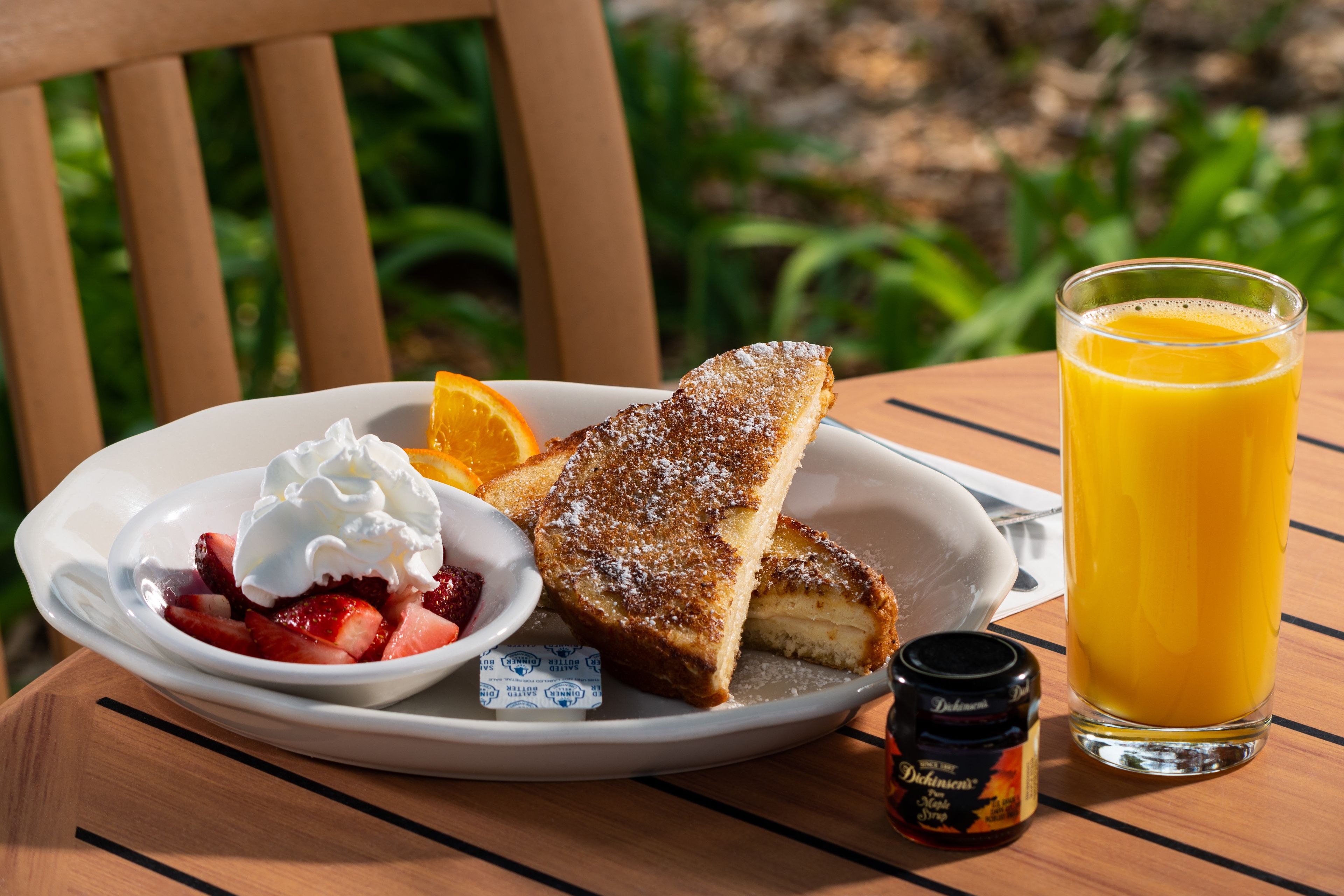 Une assiette de petit-déjeuner avec des toasts, des fraises, de la crème fouettée et un verre de jus d’orange, le tout posé sur une table en bois.