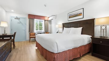 Une chambre d’hôtel avec un lit, un bureau, une chaise, une fenêtre avec des rideaux et un tableau encadré au mur.