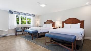 A hotel room with two beds, a chair, a table, and a window with a view.