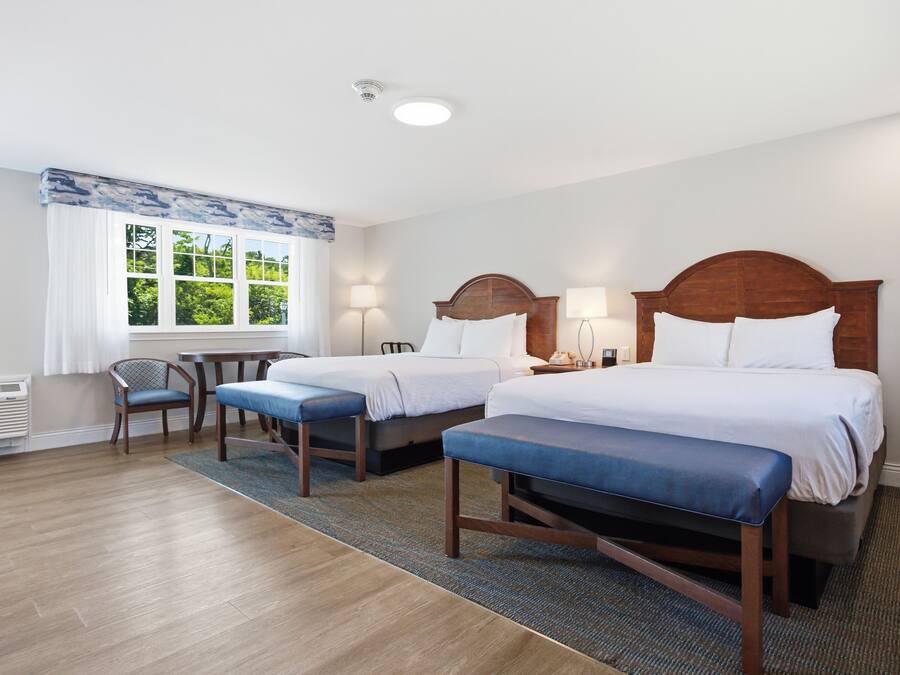 A hotel room with two beds, a chair, a table, and a window with a view.