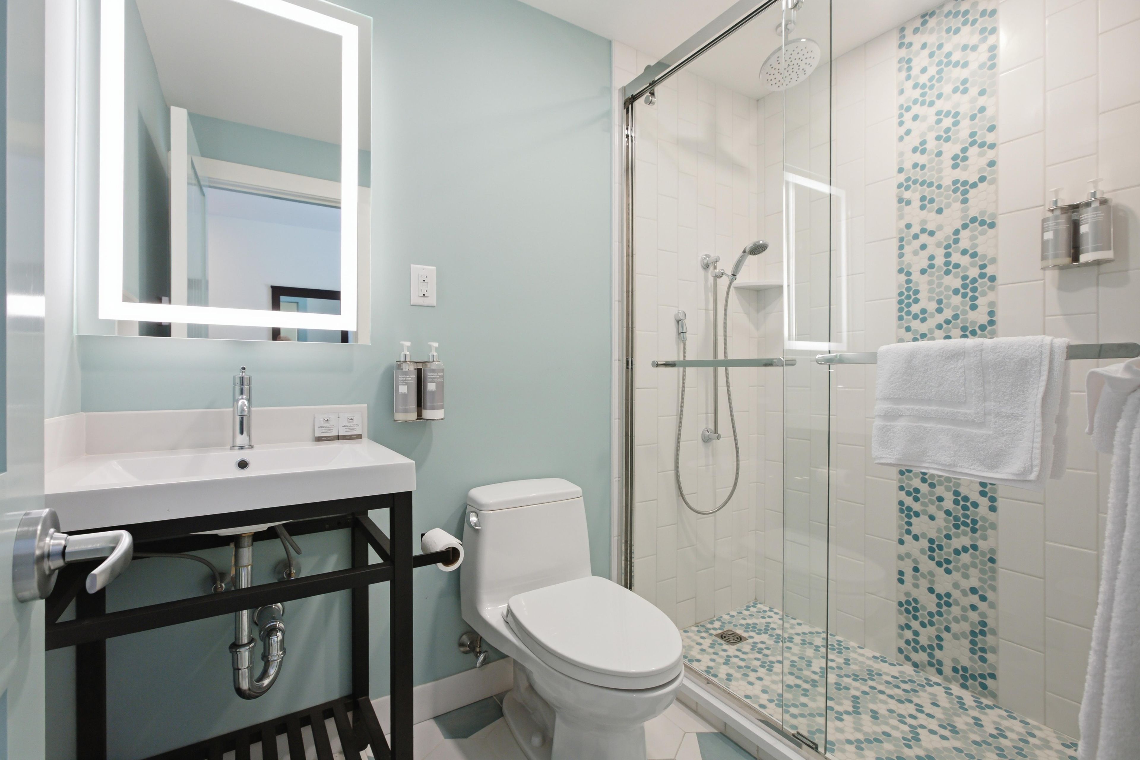 A modern bathroom with a white sink, a toilet, a glass-enclosed shower, and a mirror with a light.