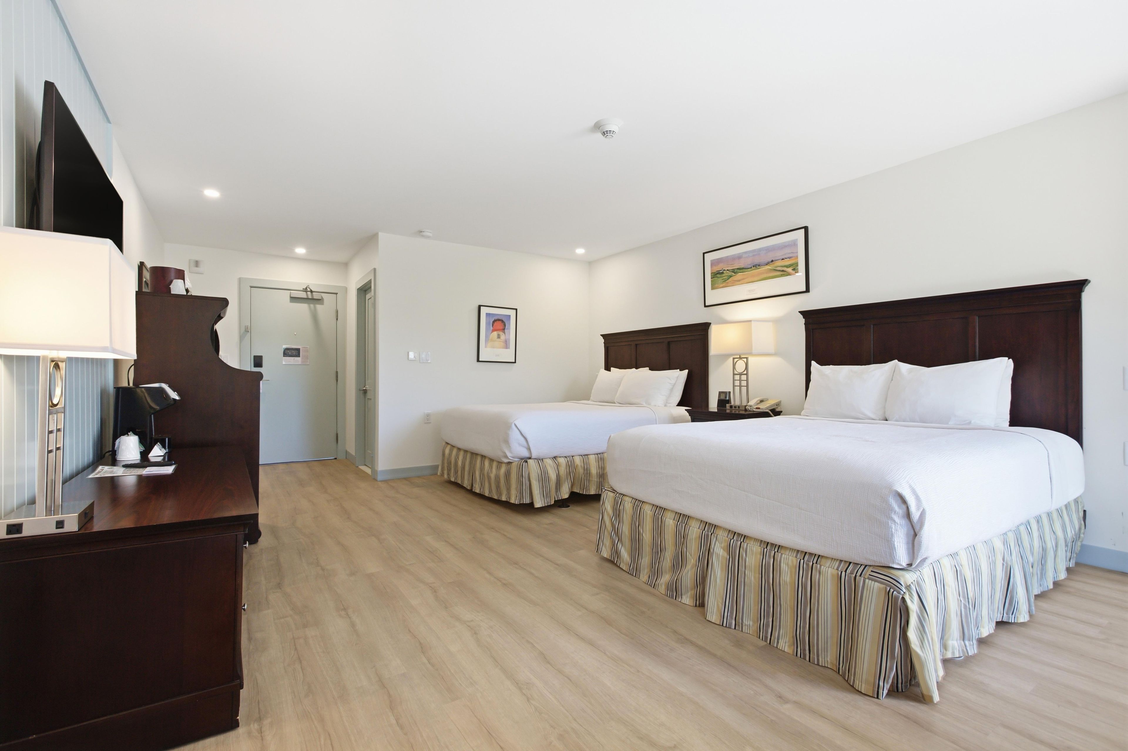 Habitación de hotel con dos camas, un escritorio, una silla, una lámpara y un cuadro en la pared.