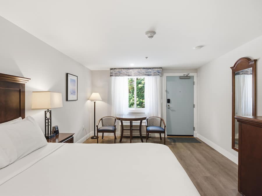 Una habitación de hotel con una cama, dos sillas, una mesa, un escritorio, un espejo y una puerta que da a otra habitación.