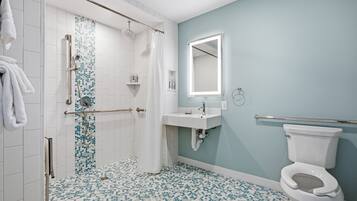 A bathroom with a shower, toilet, sink, and a mirror.