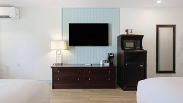 Ett hotellrum med en platt-TV som är monterad på väggen, en mörk byrå i trä med lådor, en kaffebryggare och en mikrovågsugn. Det finns två sängar med vita sängkläder.