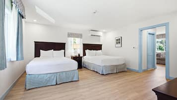 A hotel room with two beds, a nightstand, a lamp, an air conditioning unit, and a door leading to another room.