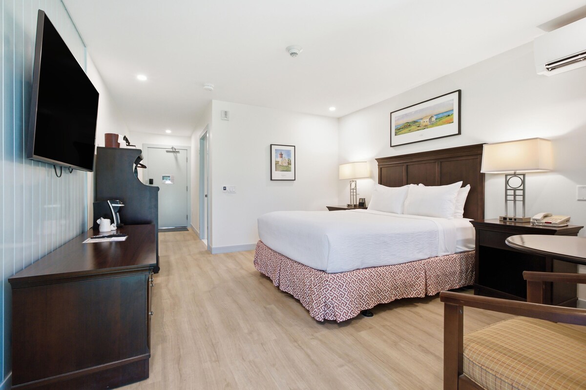 A hotel room with a bed, desk, chair, and a television.