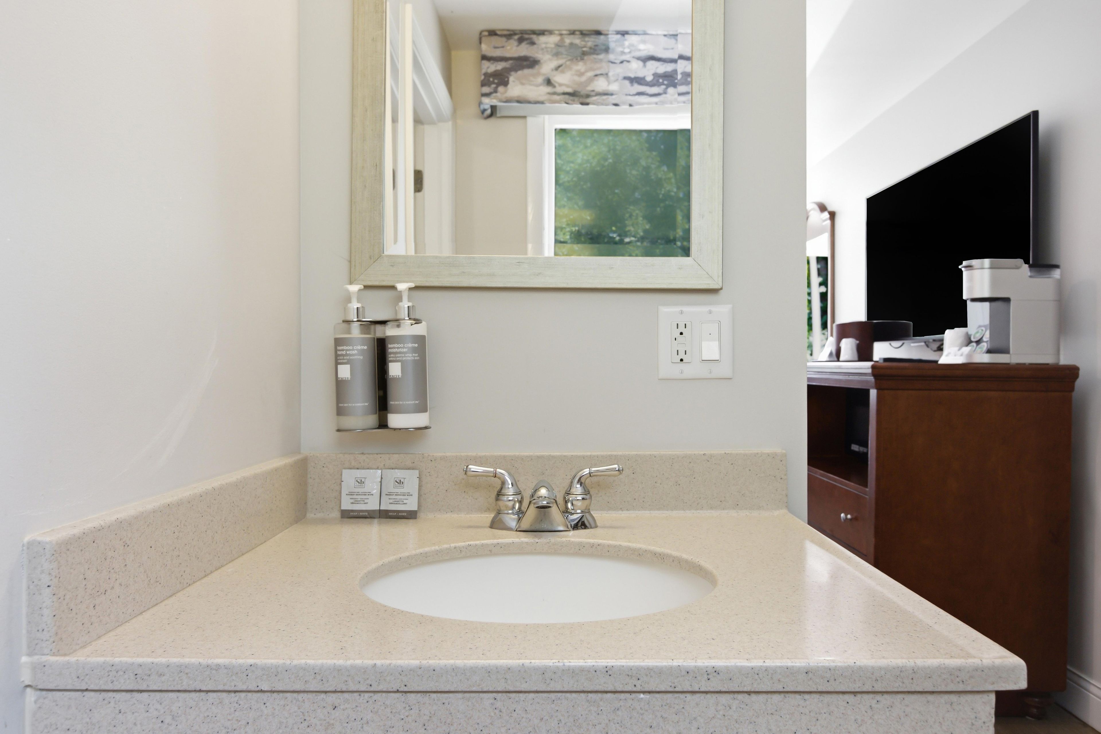 A bathroom with a white sink, a mirror above it, and a coffee machine on the right.