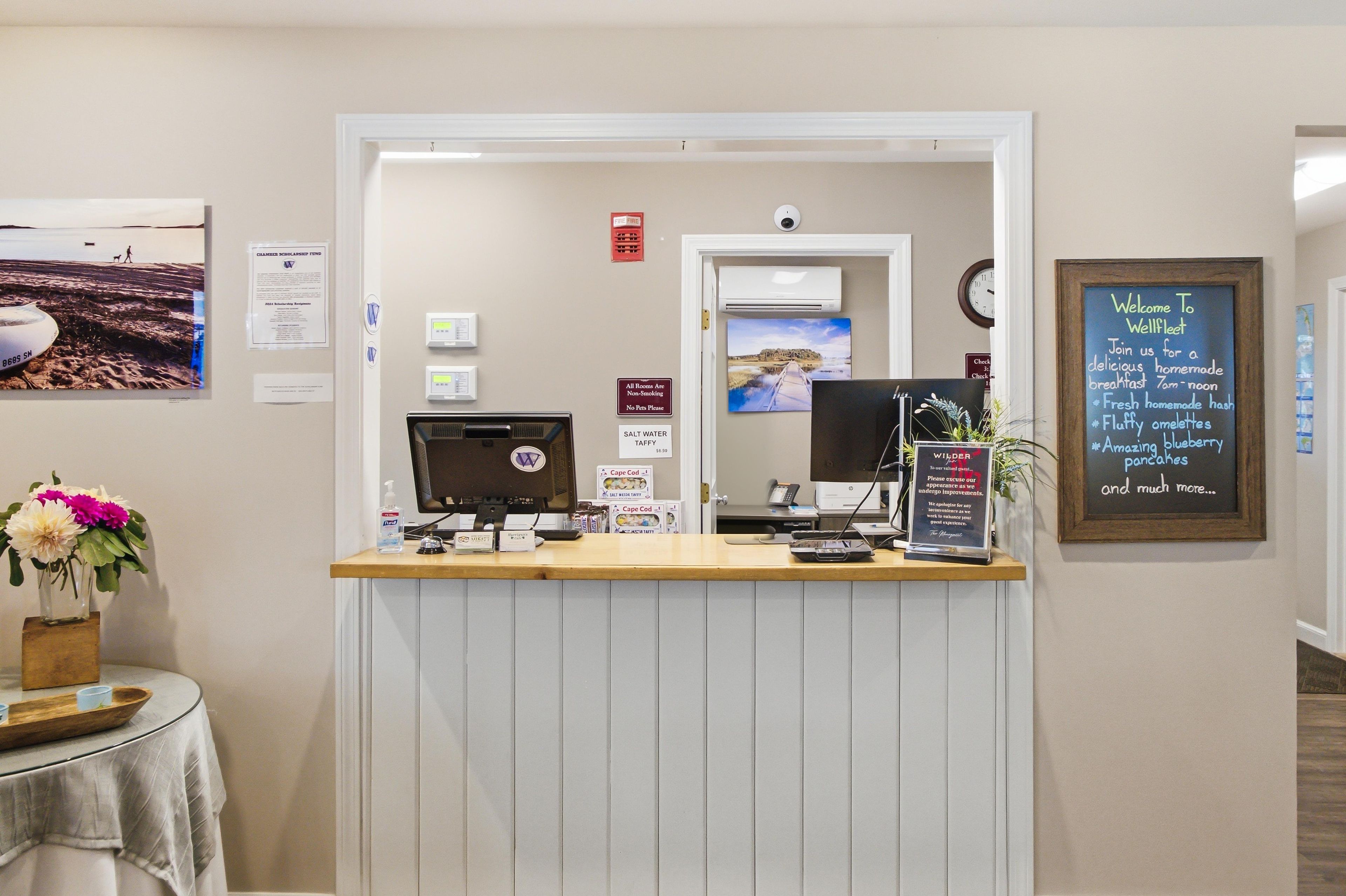 A reception desk with a computer, a phone, and a signboard. There are wall decorations and a clock.