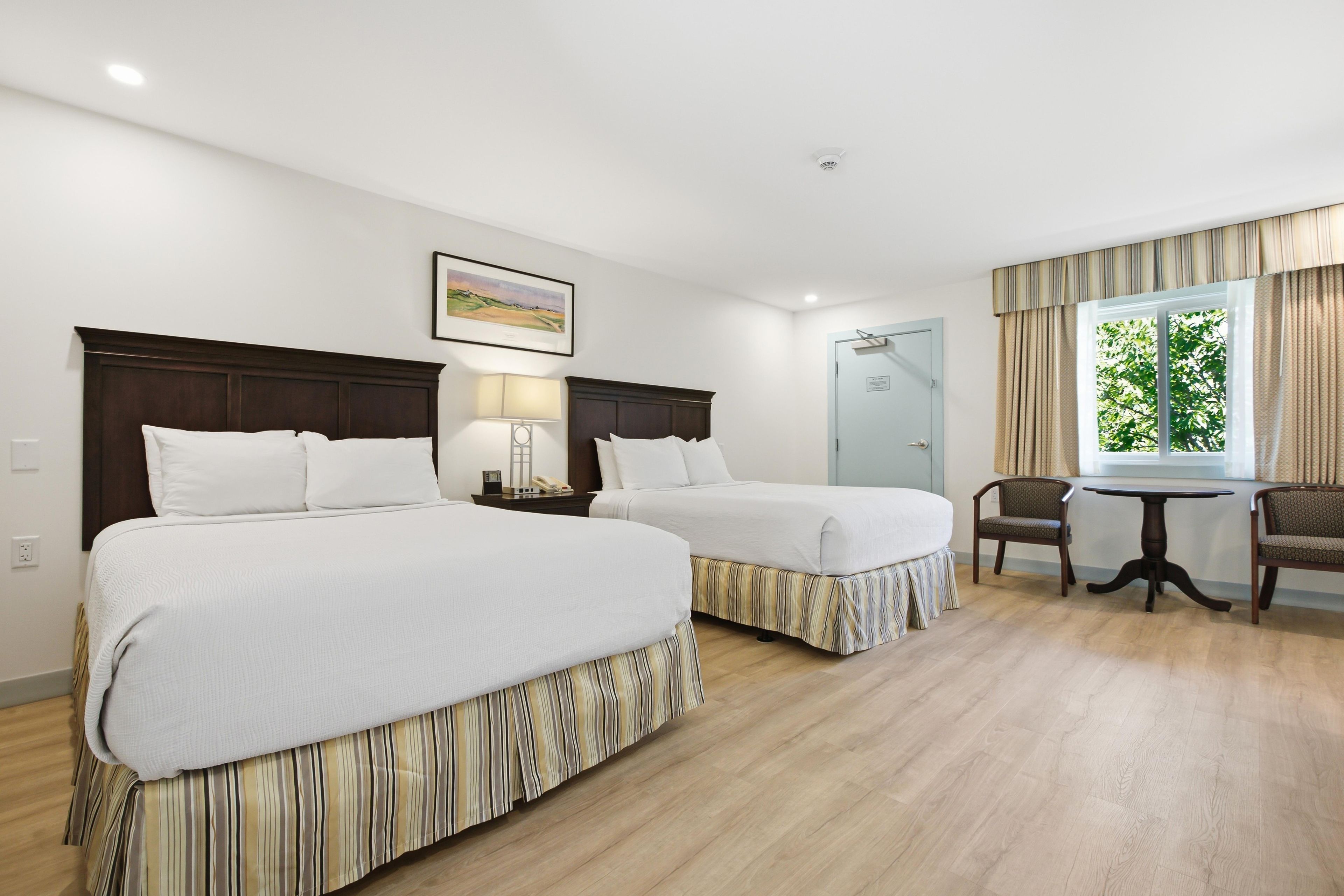 Habitación de hotel con dos camas, un escritorio, una silla y un ventanal con cortinas.