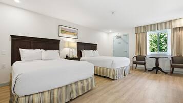 Habitación de hotel con dos camas, un escritorio, una silla y un ventanal con cortinas.