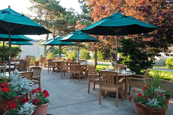 An outdoor patio area with tables and chairs, green umbrellas, and potted plants.