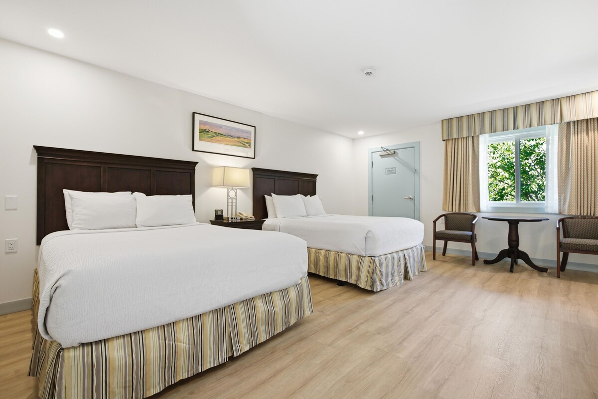 A hotel room with two beds, a desk, a chair, and a window with curtains.