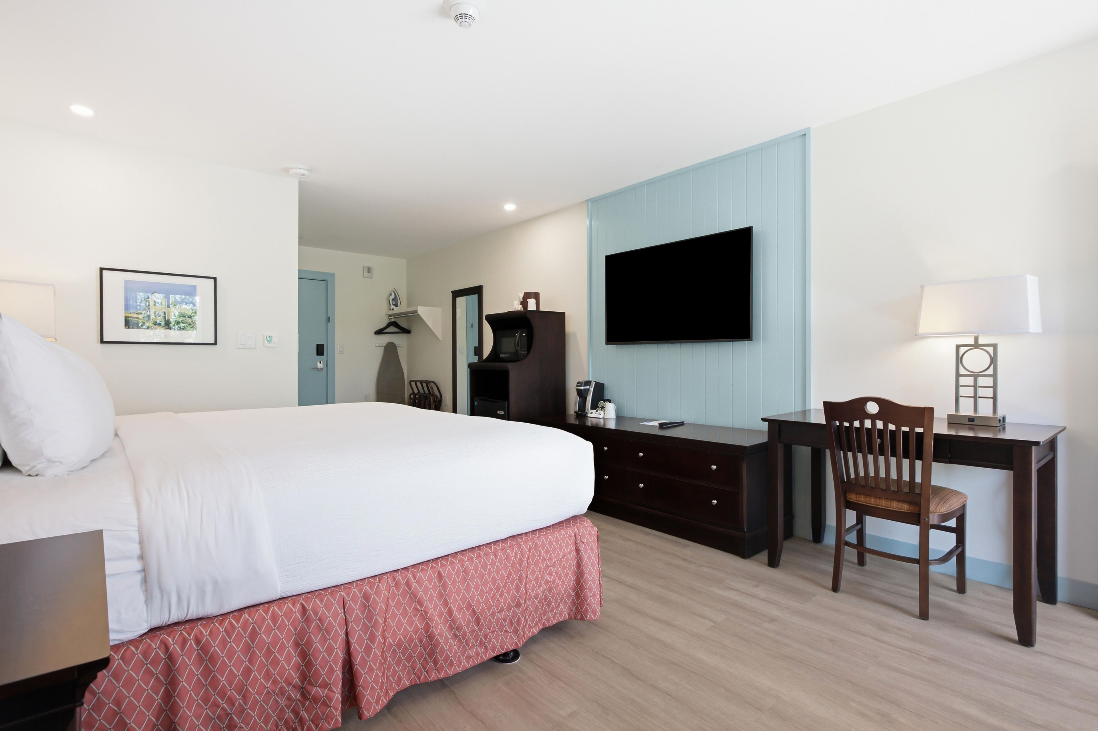 Habitación de hotel con cama, escritorio, silla, televisor de pantalla plana, lámpara y un cuadro en la pared.
