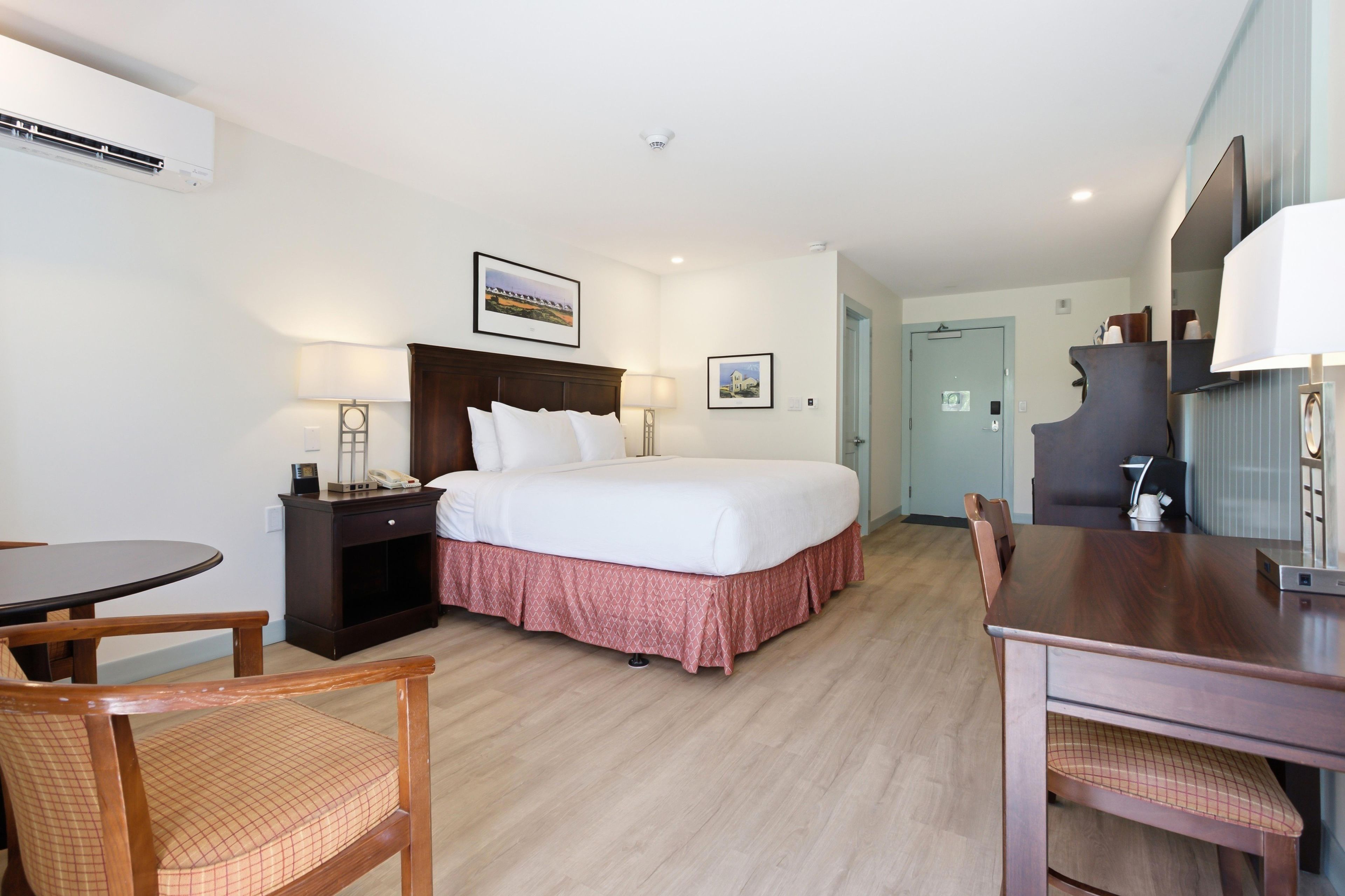 Una habitación de hotel con cama, mesita de noche, lámpara, silla y un escritorio con otra silla.