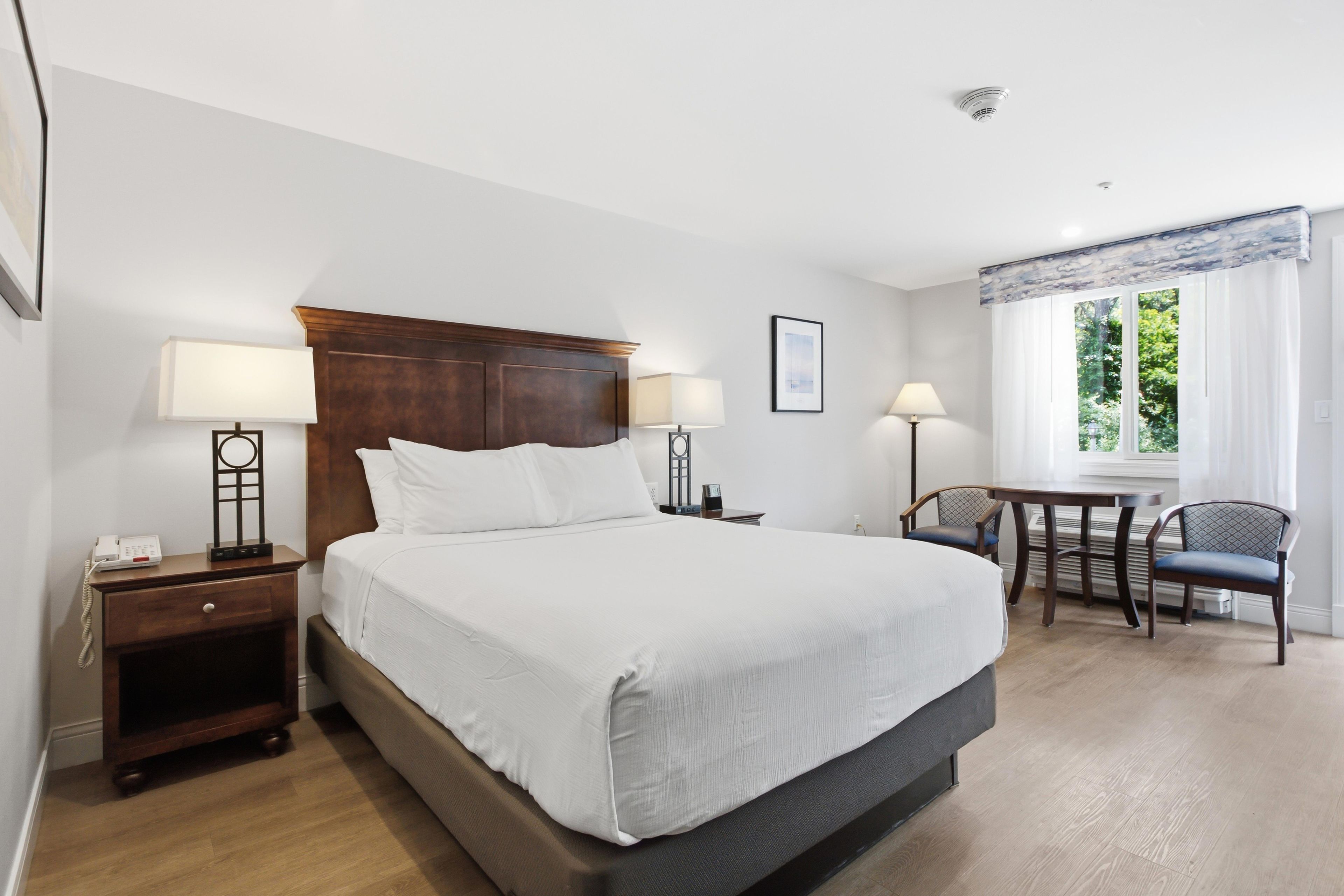 Une chambre d’hôtel avec un grand lit, des lampes de chevet, un bureau avec une chaise et une fenêtre avec des rideaux.