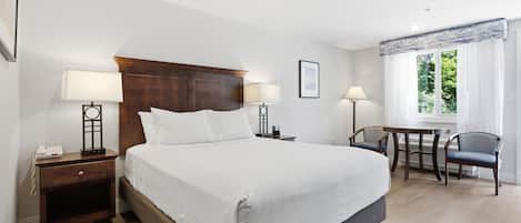 A hotel room with a large bed, bedside lamps, a desk with a chair, and a window with curtains.