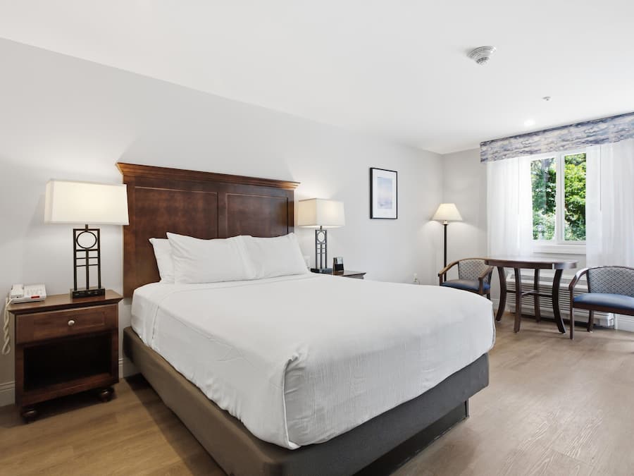Quarto de hotel com uma cama grande, abajures, uma escrivaninha com cadeira e uma janela com cortinas.
