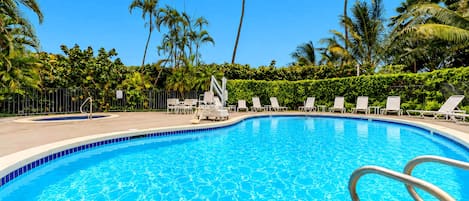 Une piscine d’un bleu éclatant, entourée de palmiers et de chaises longues.
