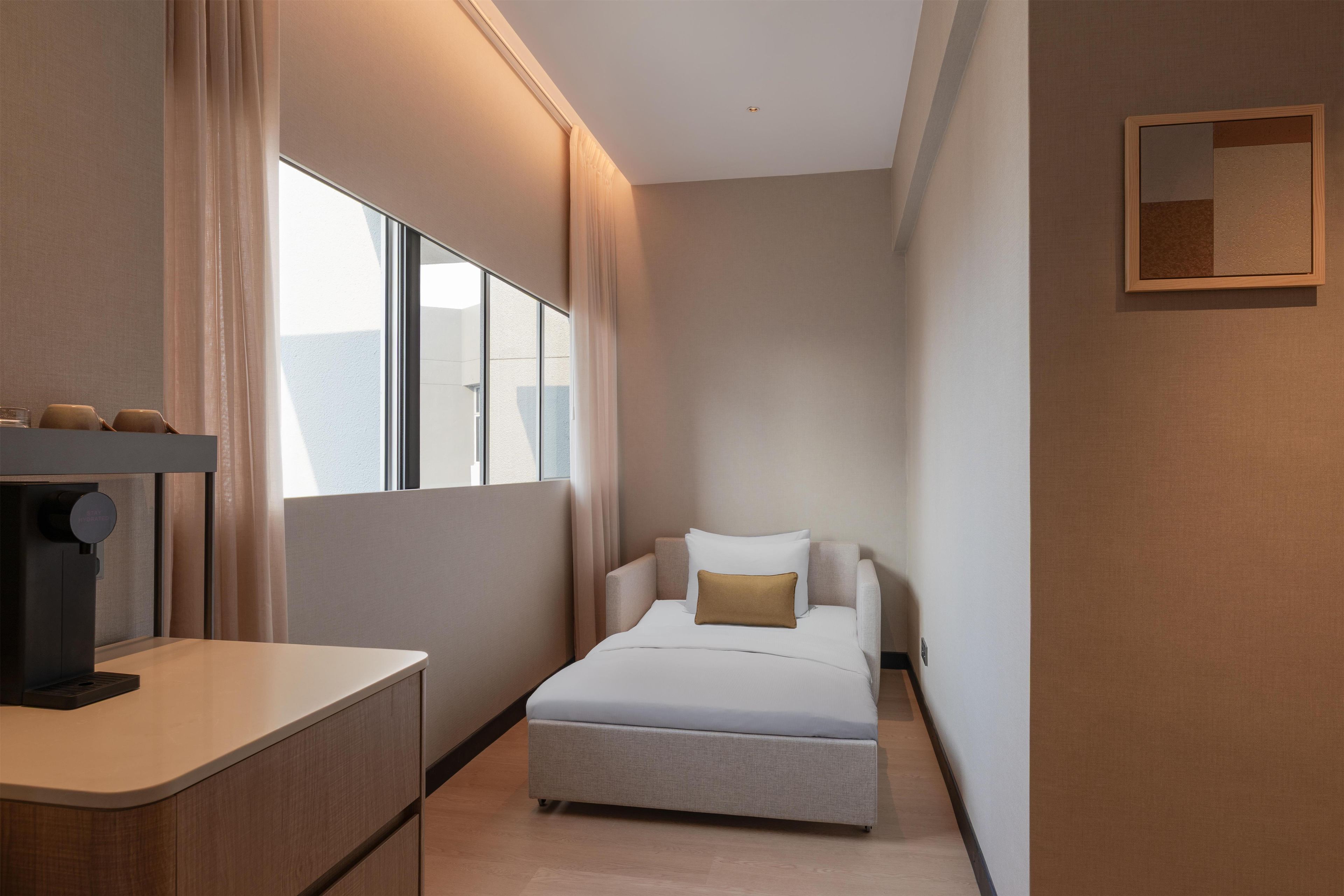 A narrow hotel room with a bed, a small desk, and a window.