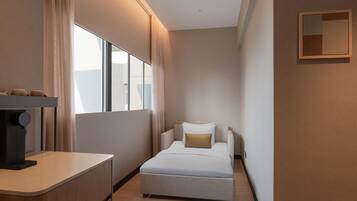 A narrow hotel room with a bed, a small desk, and a window.