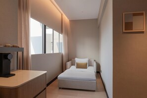 Habitación de hotel estrecha con una cama, un escritorio pequeño y una ventana.