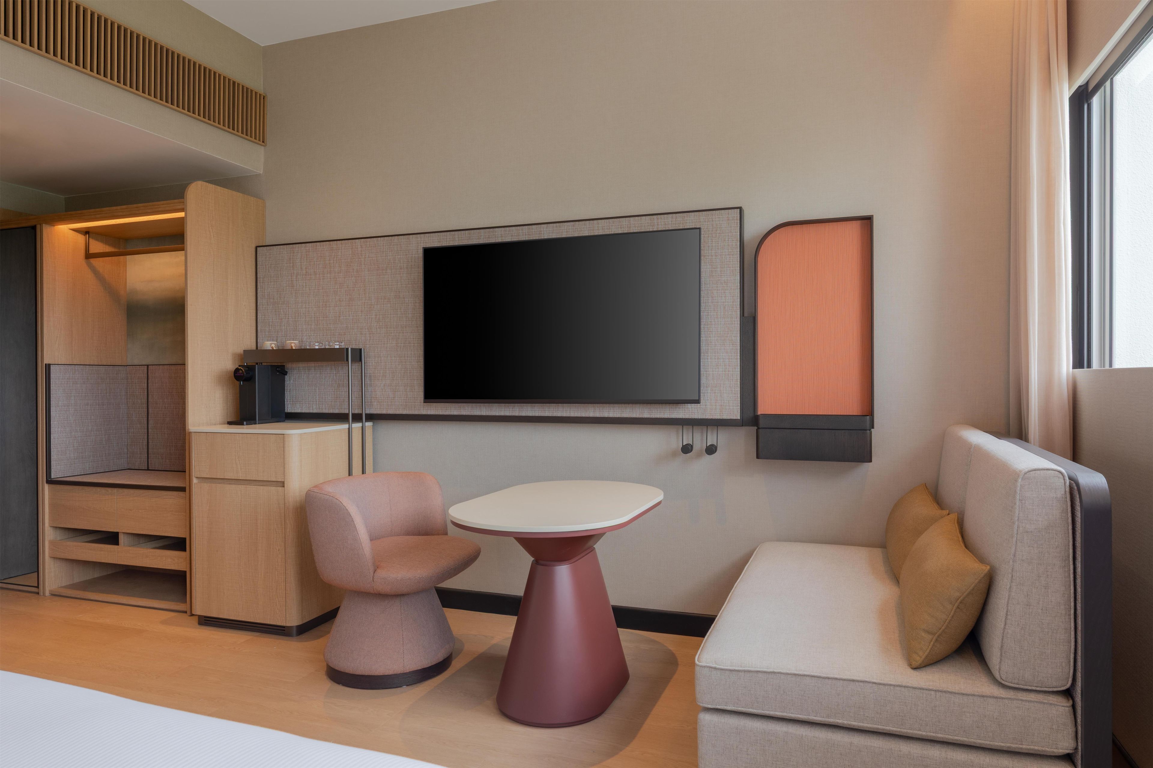Een moderne woonkamer met een flatscreen televisie aan de muur, een klein rond tafeltje en twee zithoeken met banken.