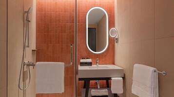 A modern bathroom with a glass shower enclosure, a round mirror with integrated lighting, and a dark wooden vanity with a white sink.