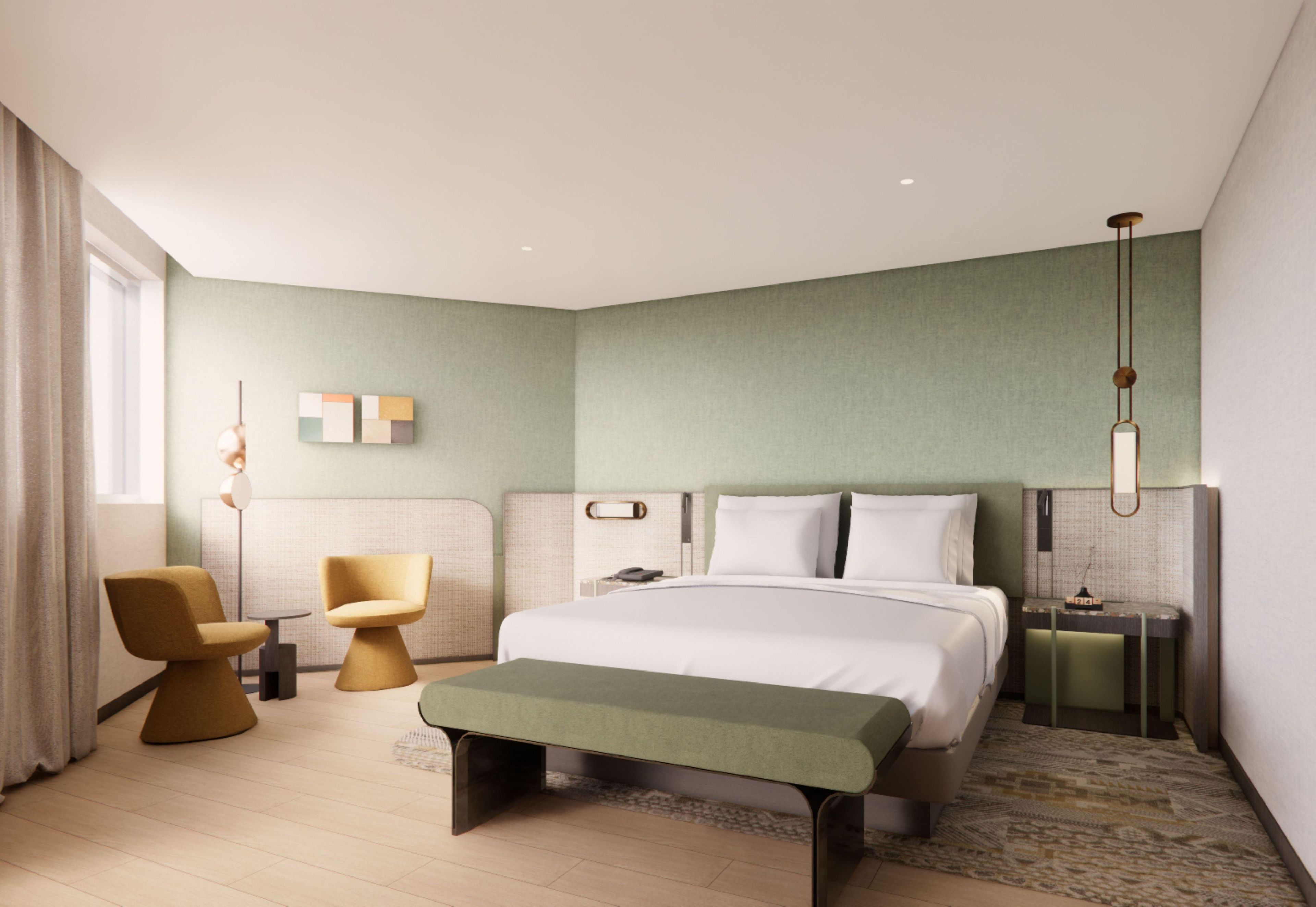 A modern hotel room with a large bed, a bench, two chairs, a bedside table, and a nightstand.