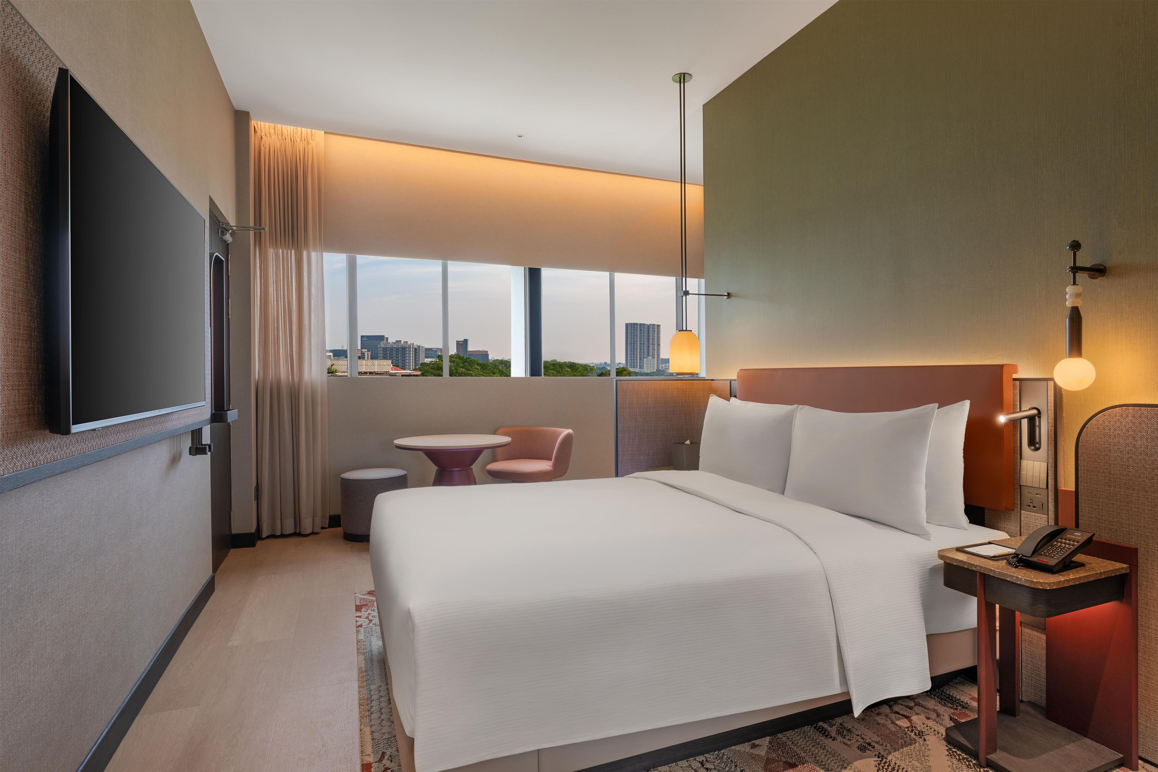 A hotel room with a bed, a desk, a chair, a TV, and a view of the city.