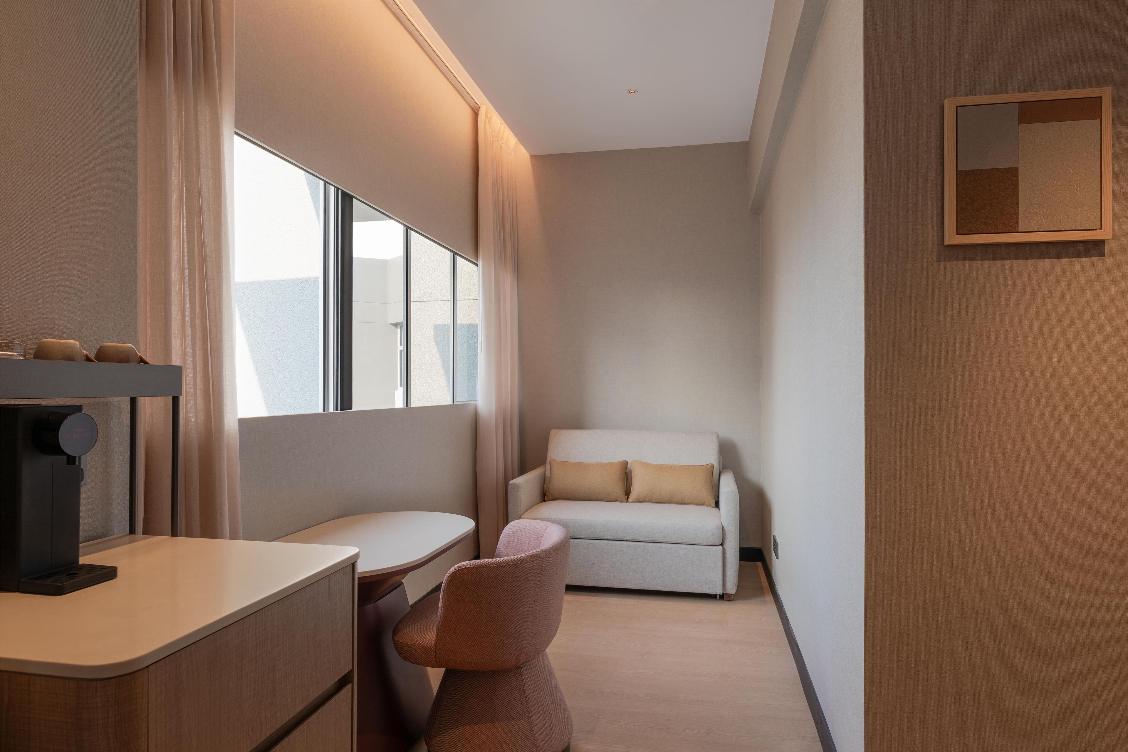 A hotel room with a desk, chair, and a sofa.