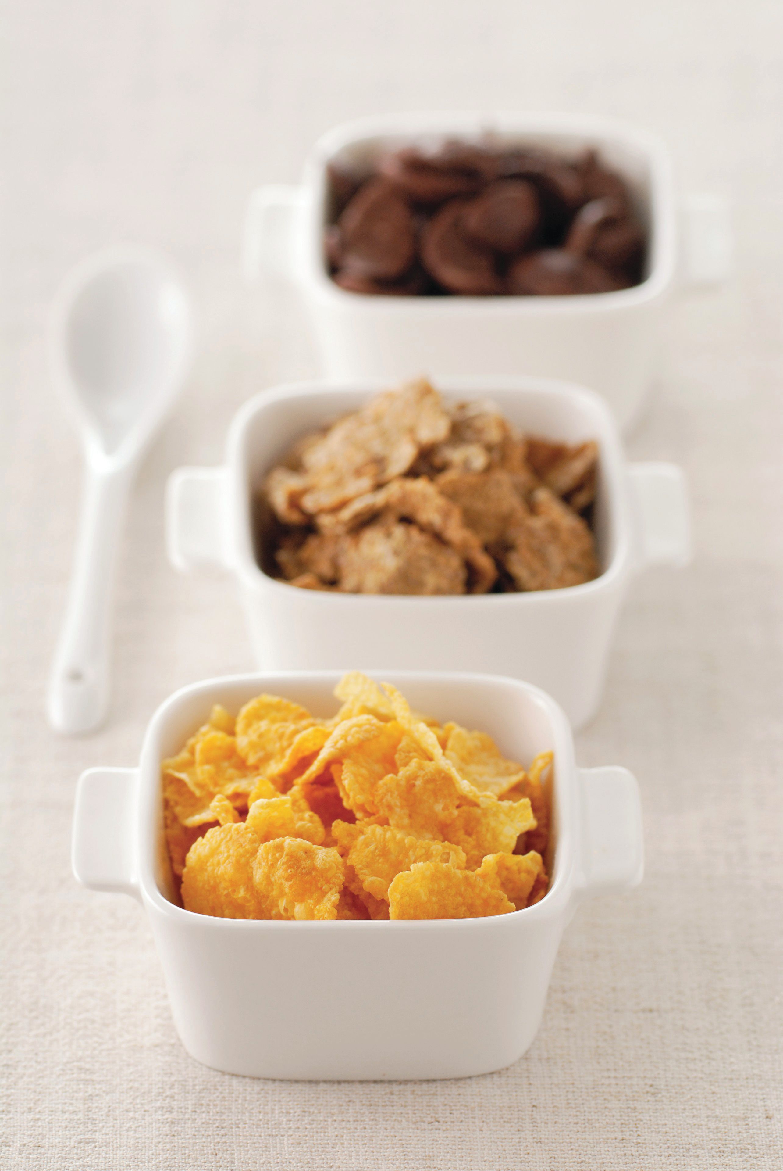 Tres tazones blancos de cerámica con asa, cada uno con un tipo diferente de cereal.