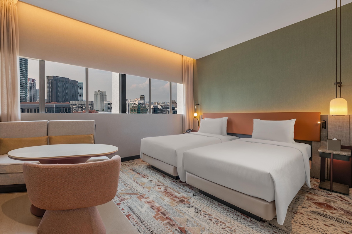 A hotel room with a city view, two beds, a small table, and a chair.