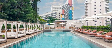A swimming pool with lounge chairs and a canopy structure, surrounded by greenery and modern buildings.