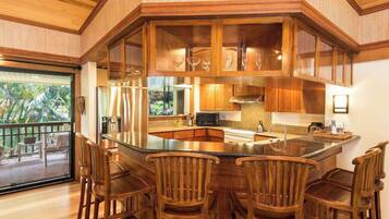 A kitchen with a central island, wooden chairs, and a view of the outdoors.