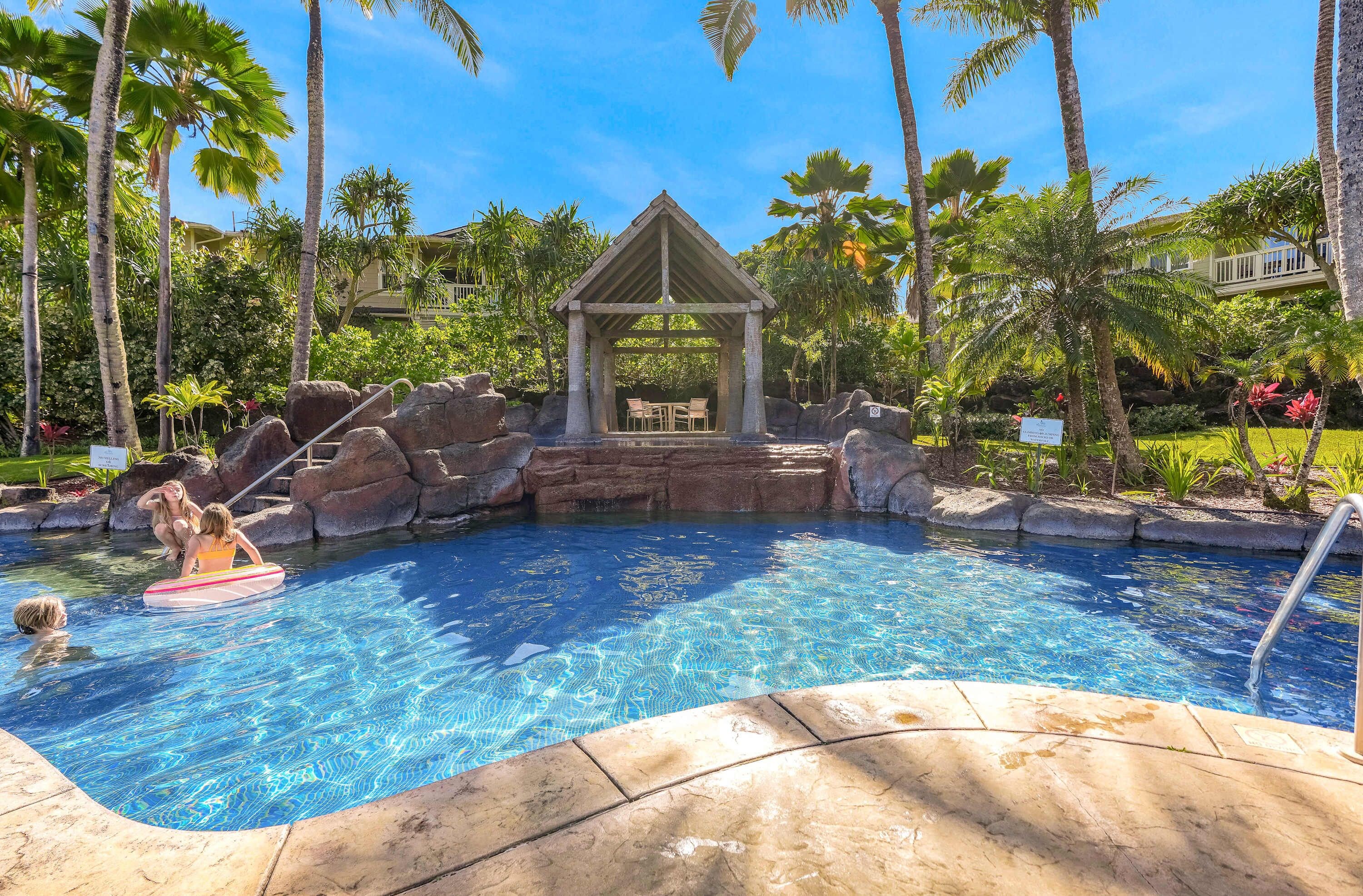 Piscina com formação rochosa e um gazebo.