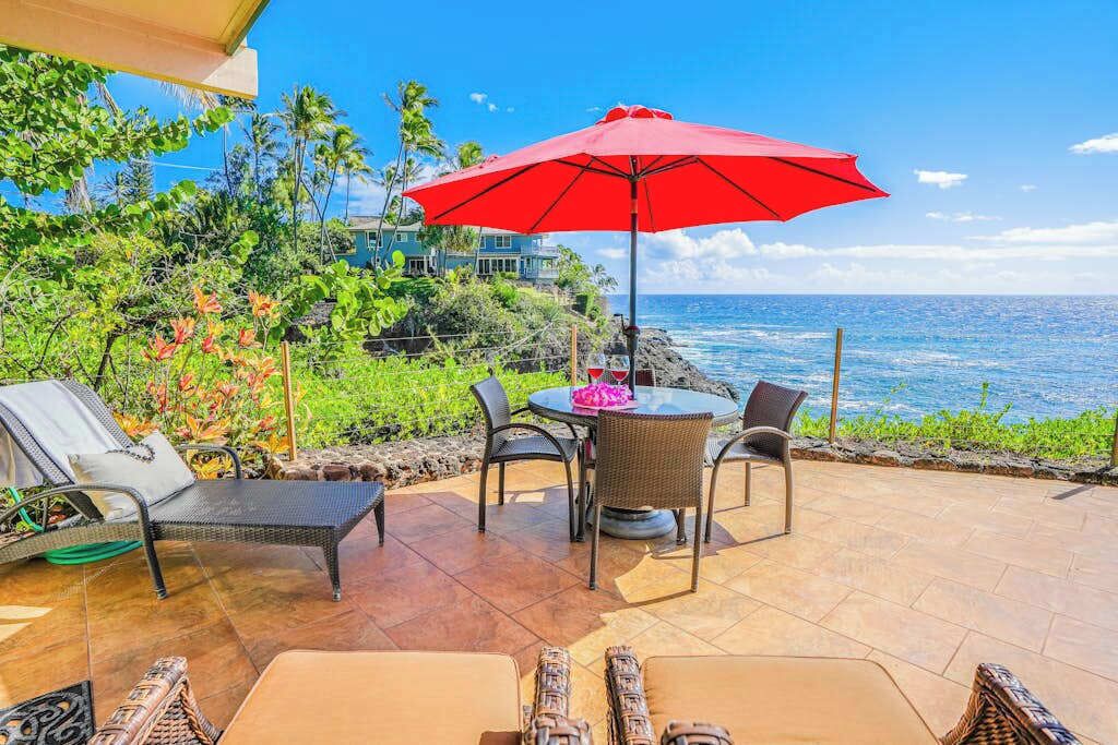 An outdoor patio with a table and chairs, a red umbrella, and a view of the ocean.