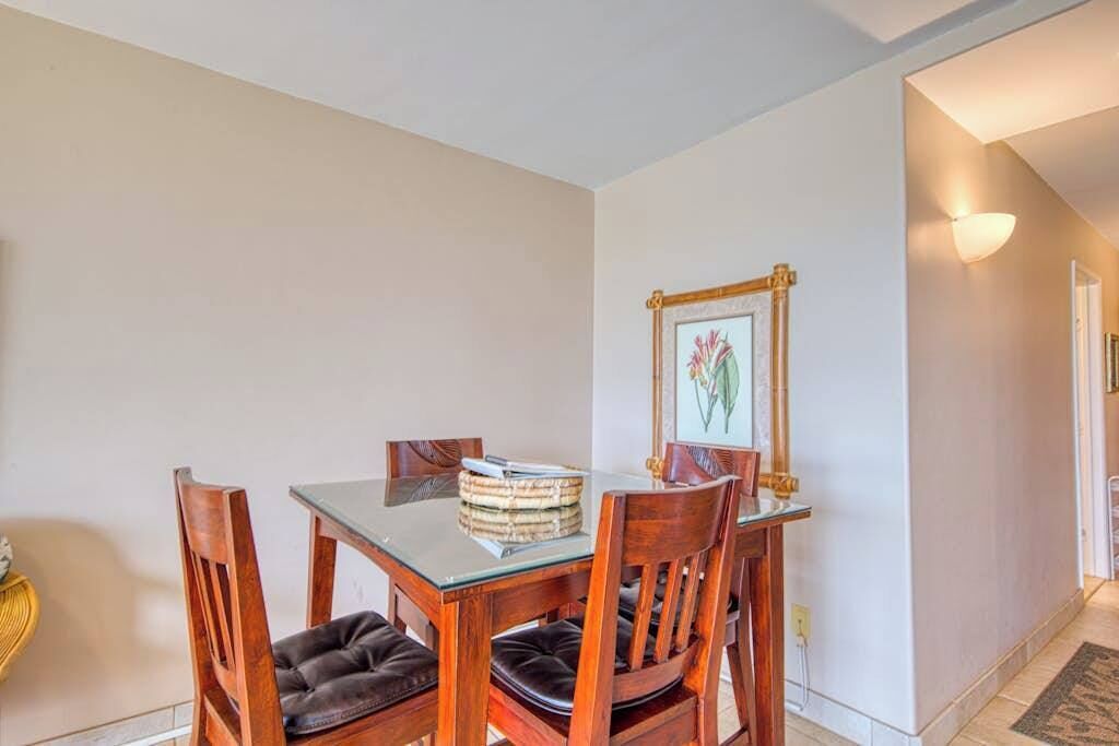 Un comedor con una mesa de vidrio, sillas de madera con asientos acolchados, un cuadro en la pared y una lámpara.
