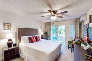 Une chambre d’hôtel équipée d’un lit, d’un bureau, d’une chaise, d’un ventilateur de plafond et d’une fenêtre avec des rideaux.