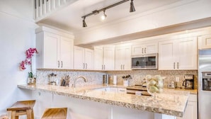Una cocina moderna con armarios blancos, encimera de granito y refrigerador de acero inoxidable.