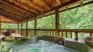 Een hottub met houten balken, een houten terras en uitzicht op bomen.